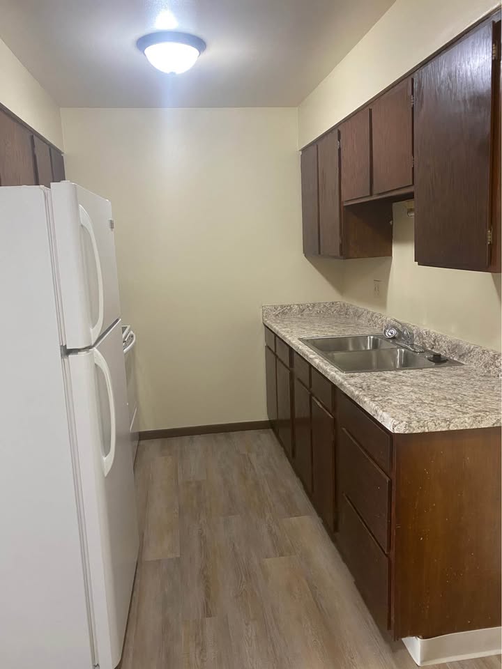 Galley kitchen with refrigerator, double sink and wood cabinetry